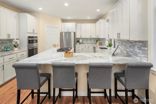 kitchen featuring tasteful backsplash, a sink, stainless steel appliances, a peninsula, and white cabinetry