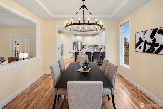 dining space featuring light wood-type flooring, baseboards, a tray ceiling, and a chandelier