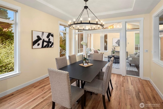 dining area featuring a raised ceiling, an inviting chandelier, light wood-style floors, and baseboards