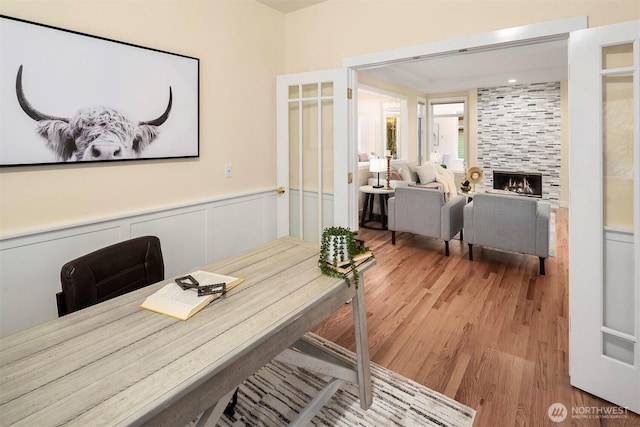 home office with a decorative wall, wood finished floors, a tiled fireplace, and a wainscoted wall