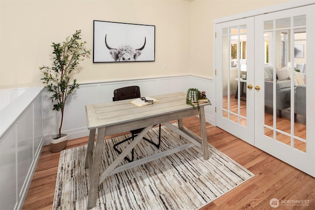 home office featuring a decorative wall, french doors, a wainscoted wall, and light wood-type flooring