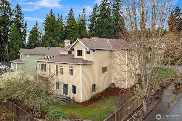 view of property exterior featuring a chimney, central AC unit, fence, a shingled roof, and a yard