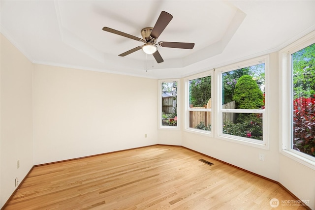 unfurnished room featuring a ceiling fan, visible vents, a raised ceiling, baseboards, and light wood finished floors