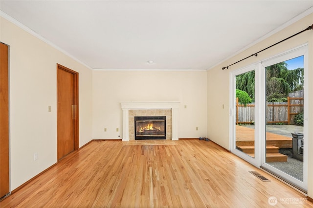 unfurnished living room featuring baseboards, light wood-type flooring, a tile fireplace, visible vents, and ornamental molding