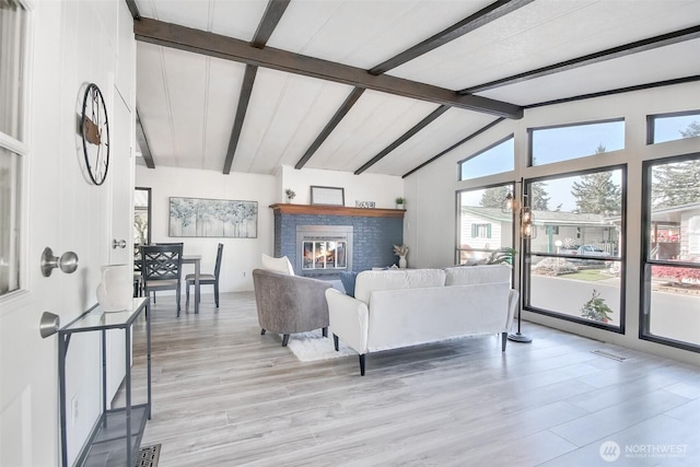 living area with a fireplace, visible vents, vaulted ceiling with beams, and light wood-type flooring