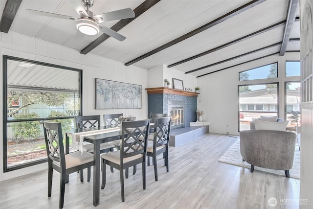 dining space with a fireplace, ceiling fan, vaulted ceiling with beams, and wood finished floors