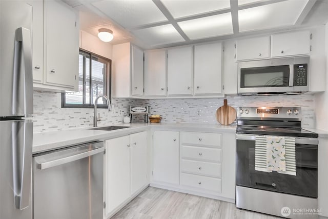 kitchen with appliances with stainless steel finishes, a sink, light countertops, white cabinetry, and tasteful backsplash