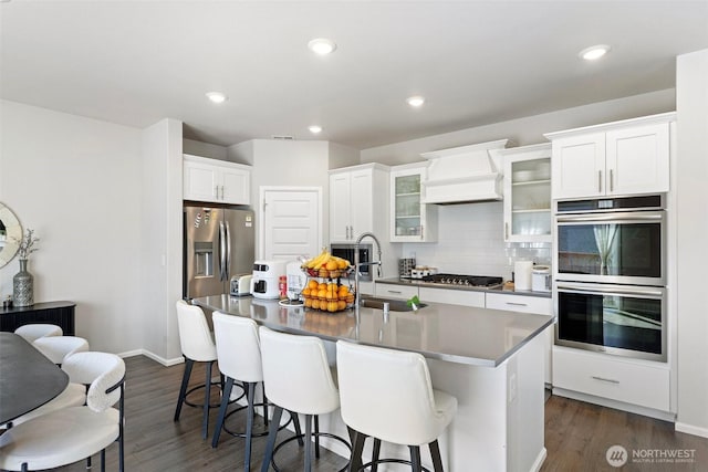 kitchen with tasteful backsplash, a sink, an island with sink, stainless steel appliances, and a kitchen bar