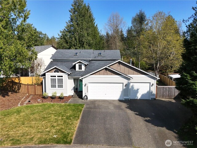 traditional-style house with aphalt driveway, fence, a shingled roof, a front lawn, and board and batten siding