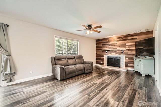 living area with wooden walls, visible vents, dark wood-type flooring, a fireplace, and ceiling fan