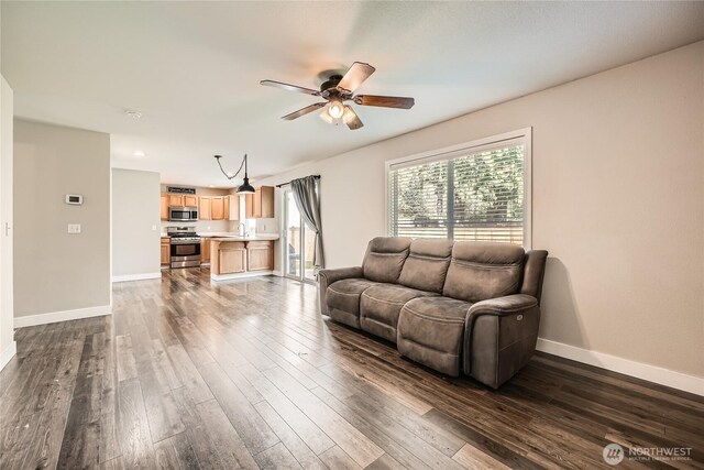 living area with a ceiling fan, baseboards, and dark wood-style flooring