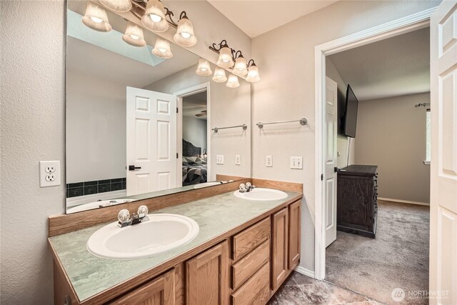 ensuite bathroom featuring ensuite bath, a sink, double vanity, and baseboards