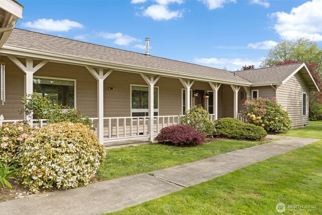 ranch-style house featuring covered porch, a front lawn, and roof with shingles