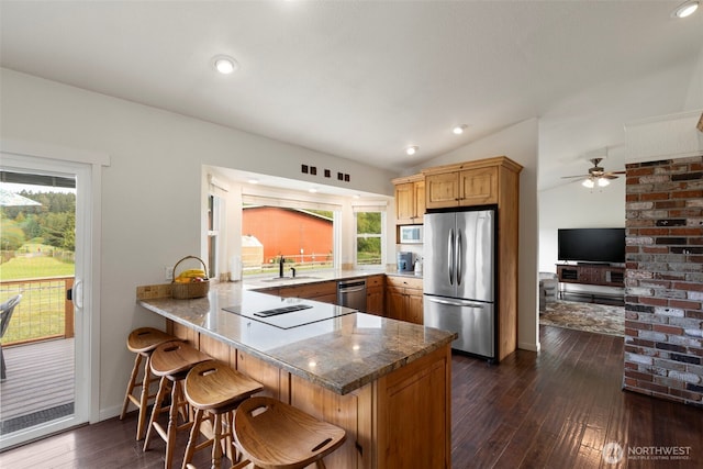 kitchen featuring stainless steel appliances, a sink, a peninsula, dark wood finished floors, and a kitchen breakfast bar