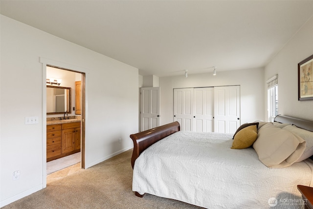 bedroom with light carpet, a sink, a closet, ensuite bath, and baseboards