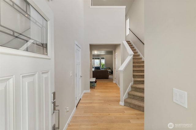 entryway with light wood finished floors, baseboards, a towering ceiling, and stairs
