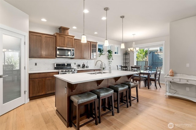 kitchen featuring stainless steel appliances, a sink, light wood-type flooring, decorative backsplash, and an island with sink
