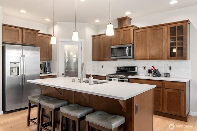 kitchen with a kitchen breakfast bar, a sink, a center island with sink, tasteful backsplash, and appliances with stainless steel finishes
