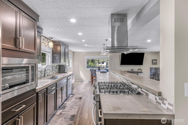 2376 Forest View Dr, Bellingham, WA 98229 - kitchen with island range hood, stainless steel appliances, dark brown cabinetry, decorative backsplash, and recessed lighting