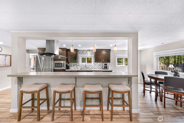 2376 Forest View Dr, Bellingham, WA 98229 - kitchen featuring island range hood, dark brown cabinets, stainless steel microwave, a breakfast bar area, and light wood-style flooring