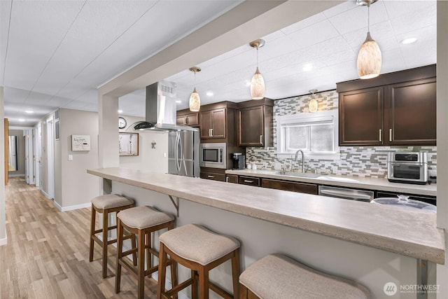 2376 Forest View Dr, Bellingham, WA 98229 - kitchen with island range hood, stainless steel appliances, a kitchen breakfast bar, dark brown cabinetry, and backsplash