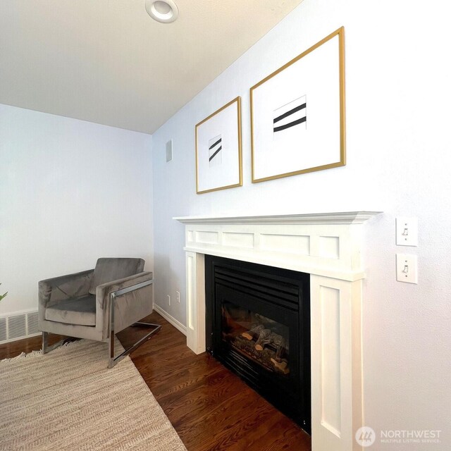 interior space featuring dark wood-type flooring, baseboards, a glass covered fireplace, and visible vents