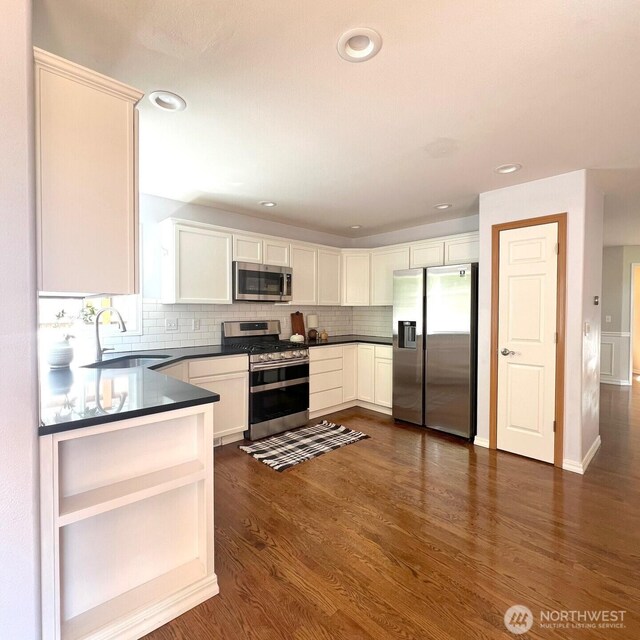 kitchen with backsplash, dark countertops, a sink, dark wood-style floors, and stainless steel appliances