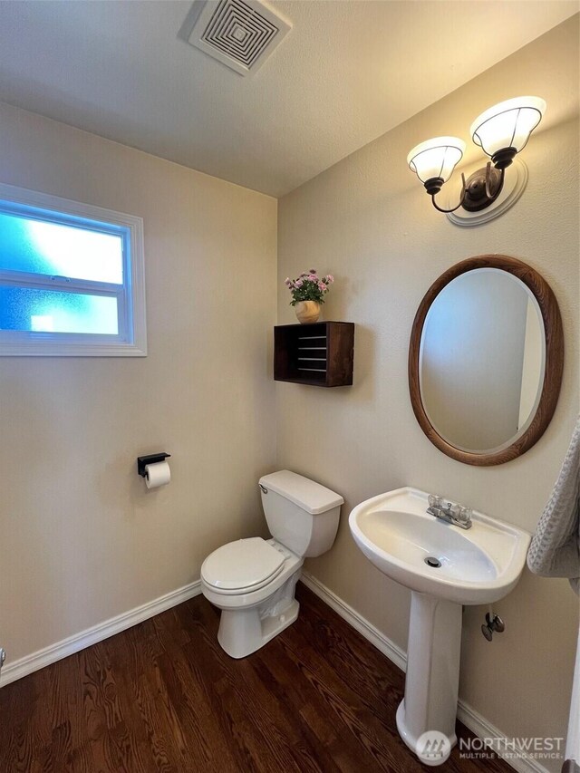 half bathroom featuring visible vents, wood finished floors, toilet, baseboards, and a sink