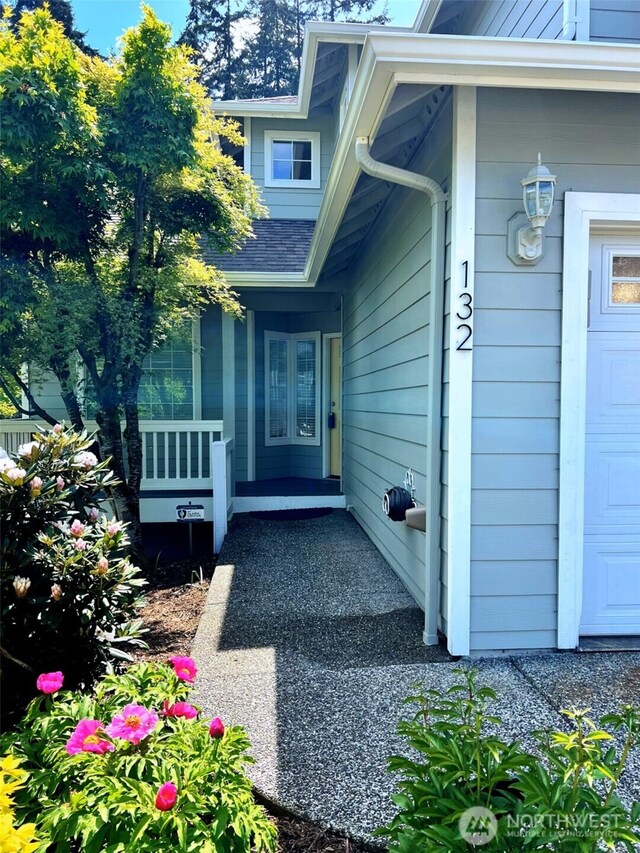 property entrance featuring a porch, a shingled roof, and a garage