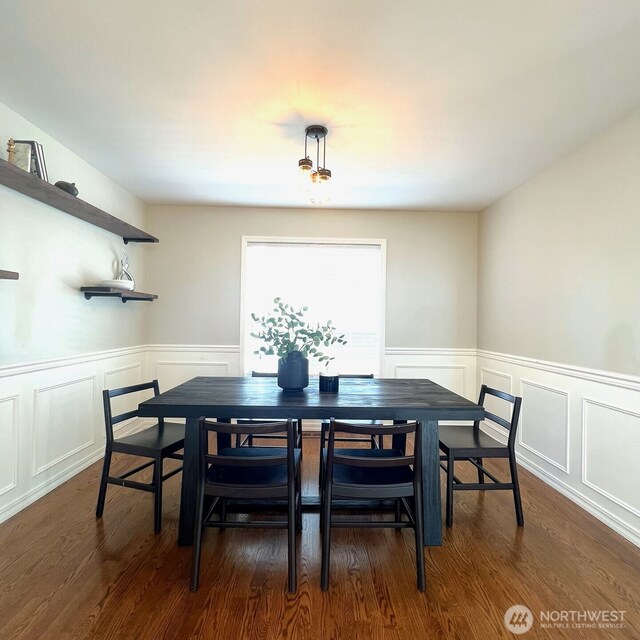 dining space featuring a decorative wall, wainscoting, and dark wood-style floors