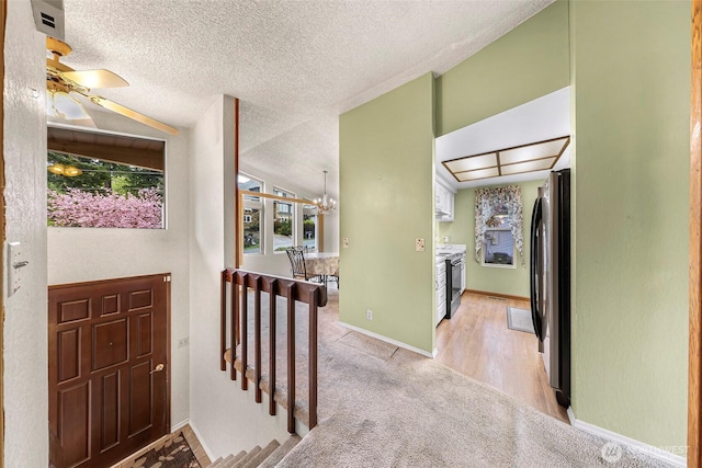 foyer featuring light colored carpet, baseboards, a textured ceiling, and ceiling fan with notable chandelier