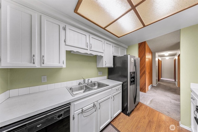 kitchen with a sink, dishwasher, light countertops, stainless steel refrigerator with ice dispenser, and white cabinetry