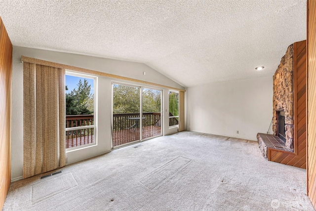 unfurnished living room with vaulted ceiling, visible vents, carpet floors, and a stone fireplace