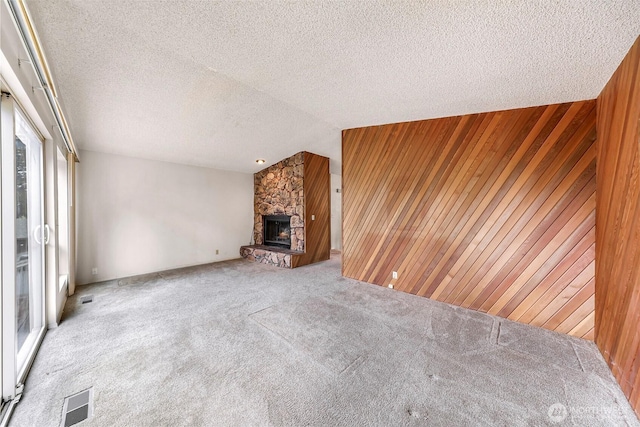 unfurnished living room with a fireplace, a textured ceiling, carpet flooring, and wood walls