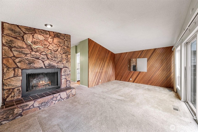 unfurnished living room featuring carpet floors, a stone fireplace, wooden walls, and a textured ceiling