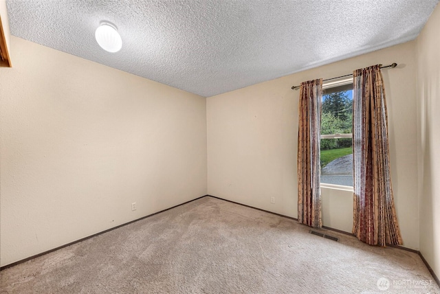 carpeted spare room featuring a textured ceiling, baseboards, and visible vents