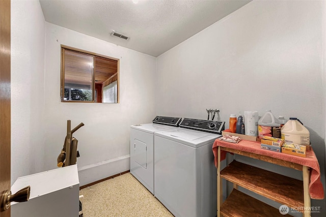 clothes washing area with laundry area, visible vents, washing machine and clothes dryer, baseboards, and a textured ceiling