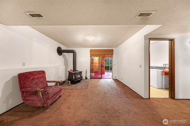 living area with a wood stove, visible vents, washer / dryer, a textured ceiling, and carpet flooring