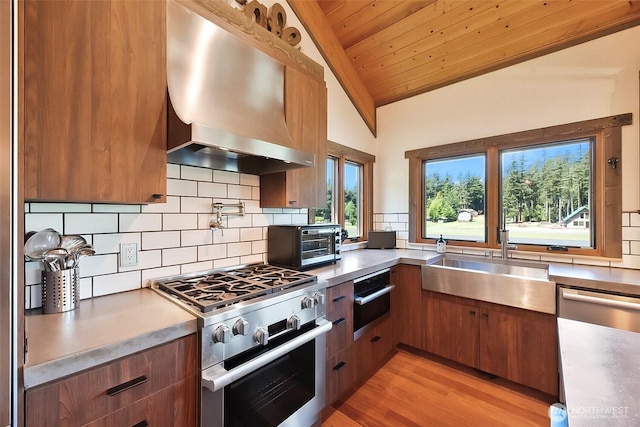 335 Blakely Dr, Blakely Island, WA 98222 - kitchen with appliances with stainless steel finishes, wall chimney range hood, a sink, tasteful backsplash, and brown cabinets