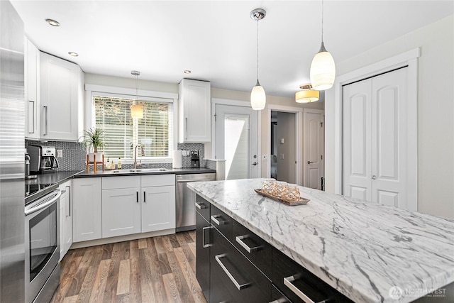kitchen featuring a sink, stainless steel appliances, wood finished floors, backsplash, and pendant lighting