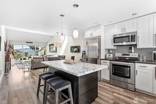 kitchen with a kitchen island, a kitchen bar, appliances with stainless steel finishes, tasteful backsplash, and wood finished floors