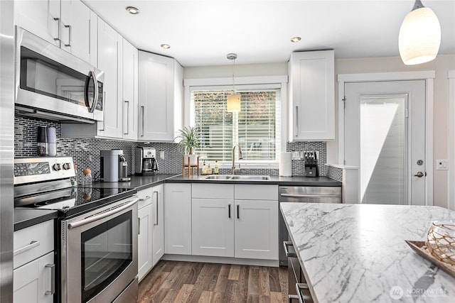 kitchen featuring dark wood-type flooring, white cabinetry, tasteful backsplash, a sink, and appliances with stainless steel finishes