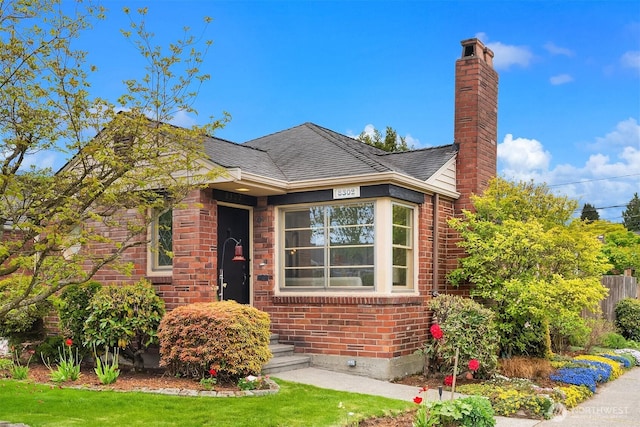 bungalow with brick siding, fence, a chimney, and roof with shingles