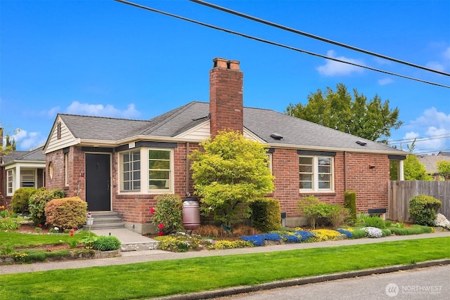 view of front of property with brick siding, fence, a chimney, and a front lawn