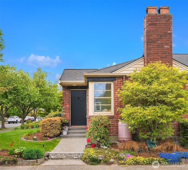 entrance to property featuring brick siding, a chimney, and a shingled roof