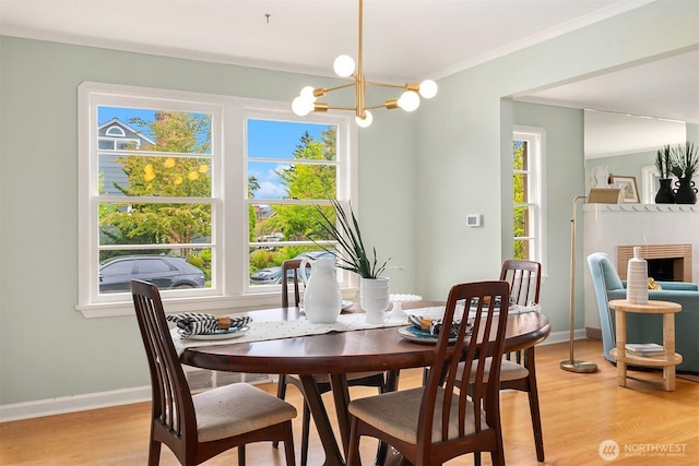 dining room featuring light wood-style floors, baseboards, a fireplace, and an inviting chandelier