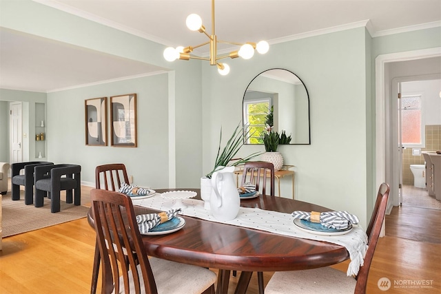 dining space with light wood-style floors, crown molding, and a notable chandelier