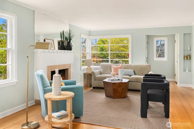 living area featuring baseboards, wood finished floors, and a warm lit fireplace