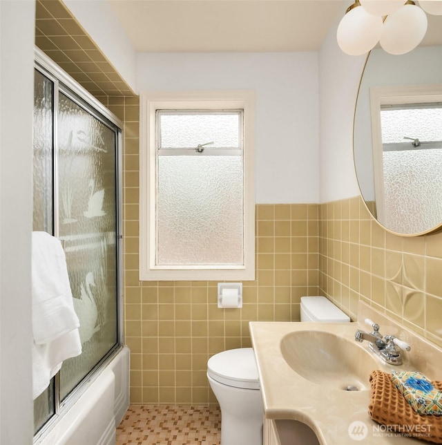 full bathroom featuring vanity, toilet, a wainscoted wall, tile walls, and combined bath / shower with glass door
