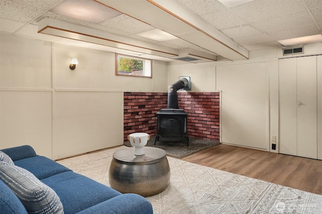 living room featuring visible vents, a paneled ceiling, a wood stove, and wood finished floors